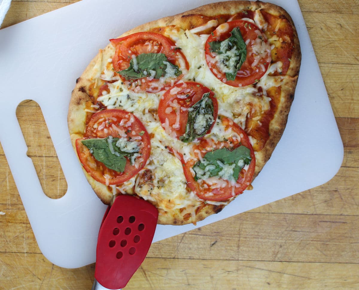 using tongs and a cutting board to remove pizza from oven