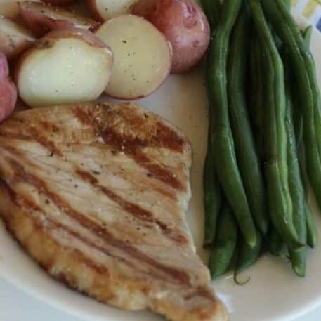 a plate with pork chops, green beens and red potatos.