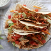 Shredded chicken tacos on a white plate. Chicken tacos contain shredded chicken, salads, pico de gallo, taco seasoning.