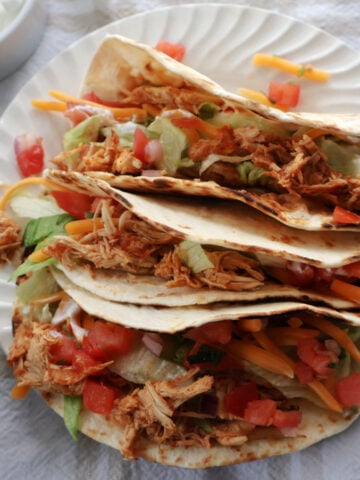 Shredded chicken tacos on a white plate. Chicken tacos contain shredded chicken, salads, pico de gallo, taco seasoning.