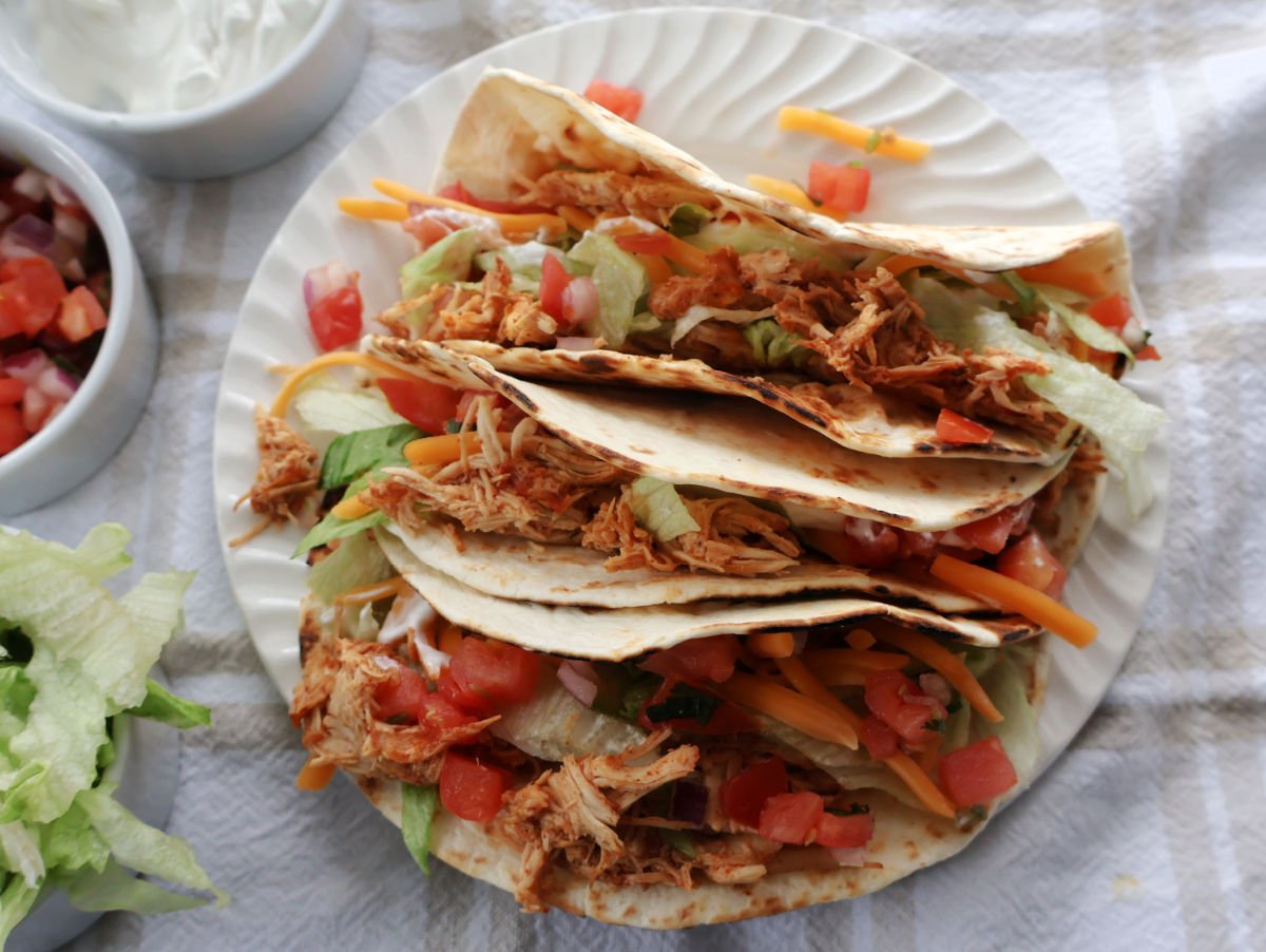 Shredded chicken tacos on a white plate. Chicken tacos contain shredded chicken, salads, pico de gallo, taco seasoning.