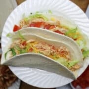 two shredded chicken tacos on a white plate.