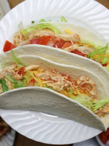 two shredded chicken tacos on a white plate.