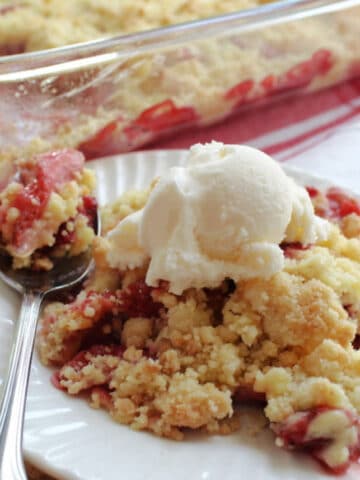 a serving of strawberry dump cake with vanilla ice cream on a white plate.