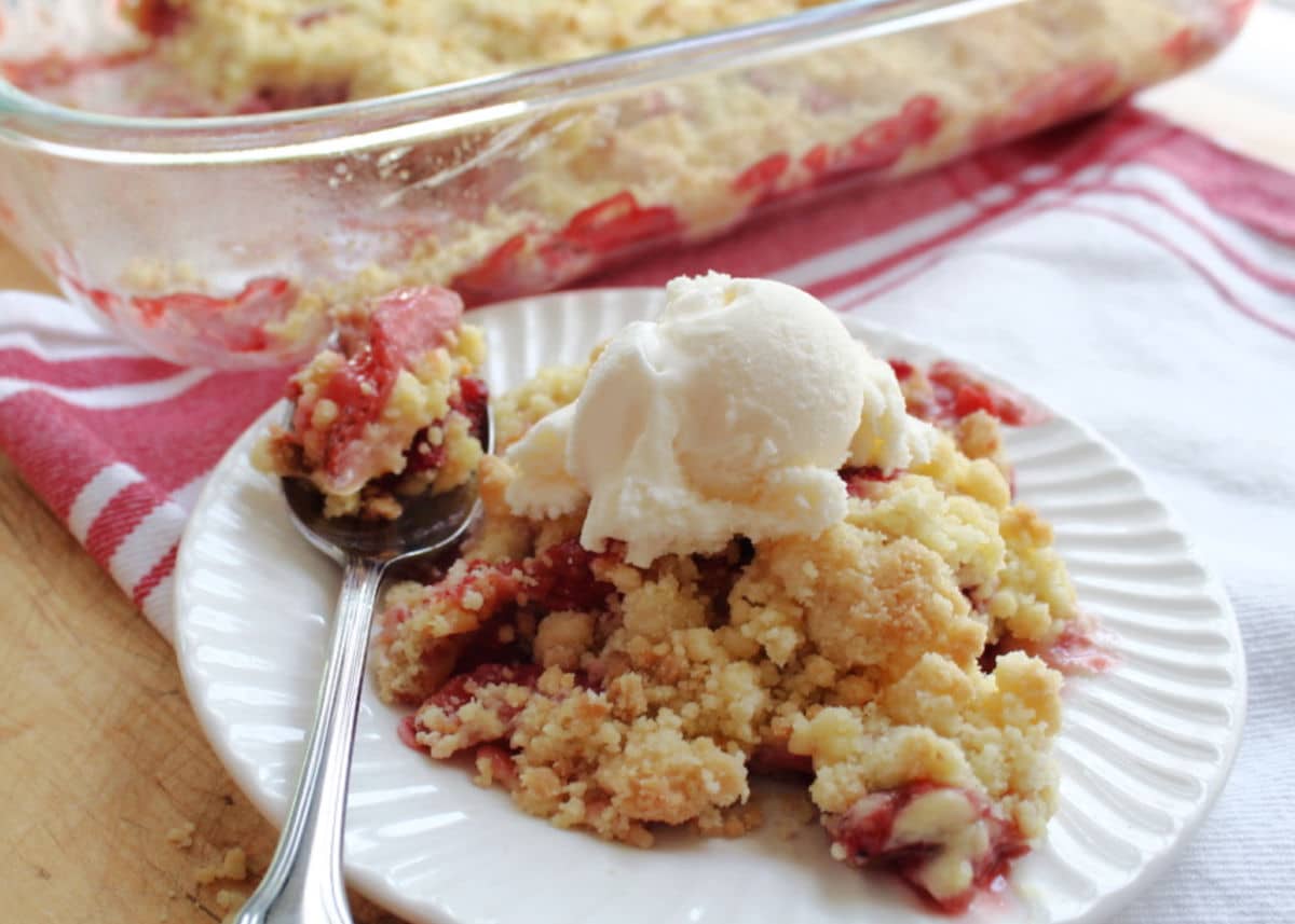 a serving of strawberry dump cake with vanilla ice cream on a white plate.