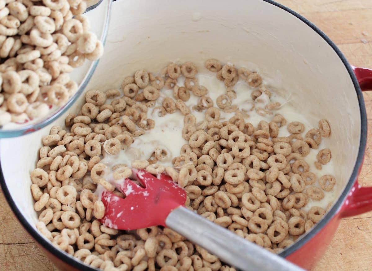 Adding Cheerios to melted marshmallows.