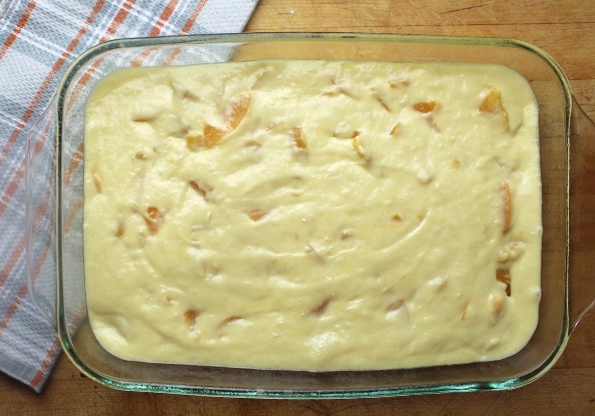 batter with sliced peaches in a baking dish .