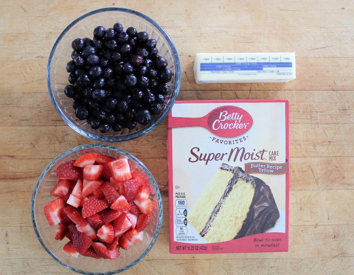 Ingredients for berry cobbler which are blueberries, chopped strawberries, cake mix and a stick of butter. 