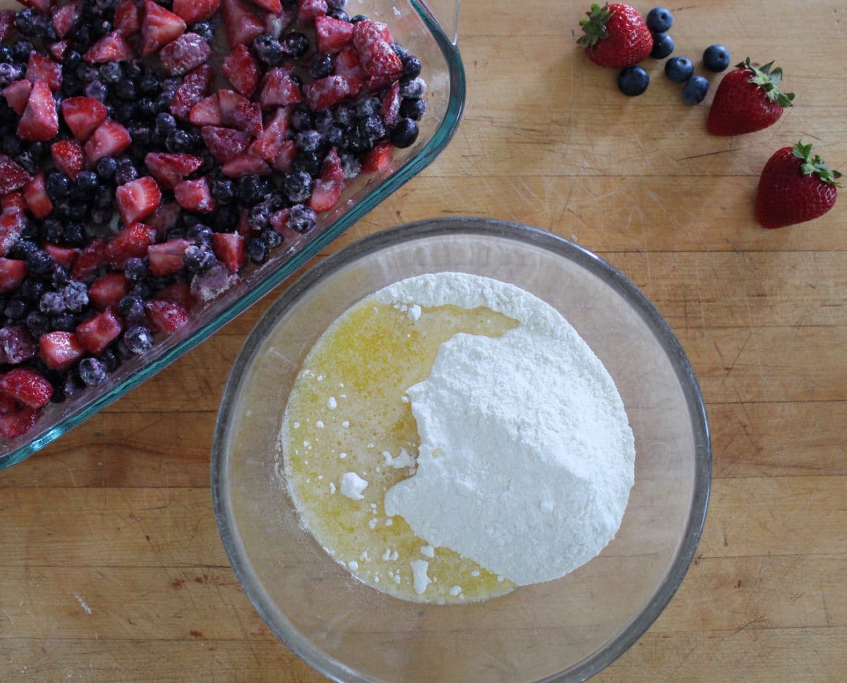 cake mix and melted butter in a bowl. Baking dish with strawberries and blueberries in the background.