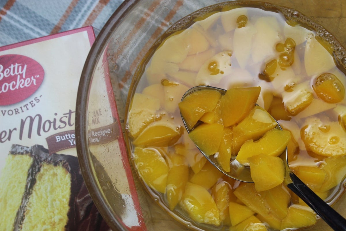 cut up sliced peaches in a large glass bowl with a box of cake mix  beside the bowl.