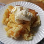 Peach dump cake with ice cream on a white plate.