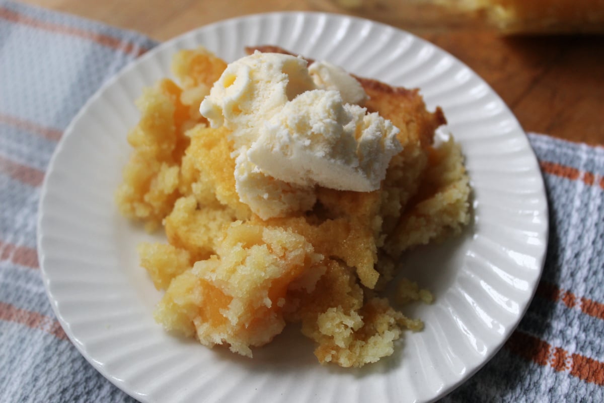 Peach dump cake with ice cream on a white plate.