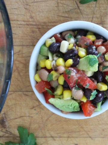 cowboy caviar in a small white bowl. the cowboy caviar contains a couple of been varieties, corn, tomatoes and peppers with optional avacado on top.
