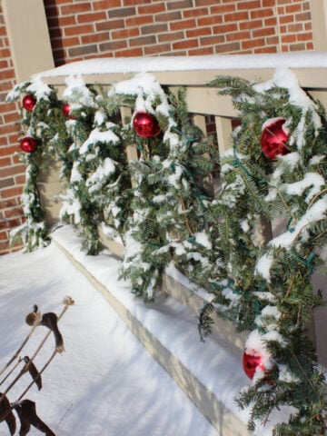 Green live garland on a porch railing with red bows