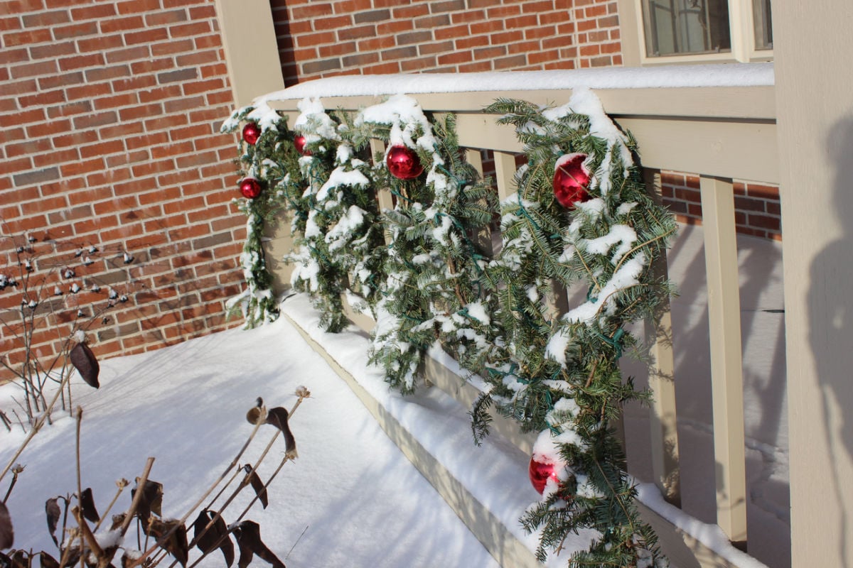 Green live garland on a porch railing with red bows