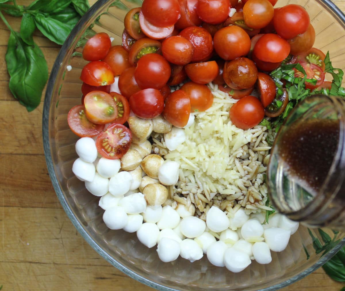 pouring dressing over caprese orzo salad.
