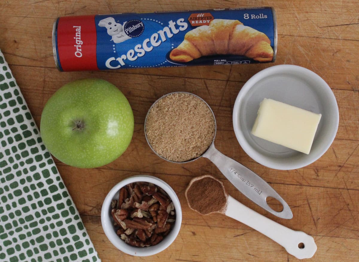 ingredients for apple pie bites which include crescent rolls, an apple, brown sugar, pumpkin pie spice butter and optional pecans.