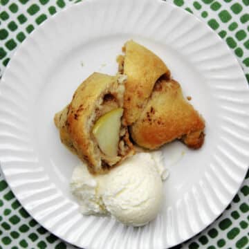 an apple pie bite cut in half with a scoop of ice cream on the white plate.