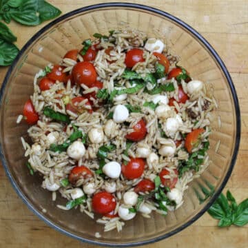caprese orzo salad with fresh tomatos, basil, small mozzarella and orzo all in a glass bowl.