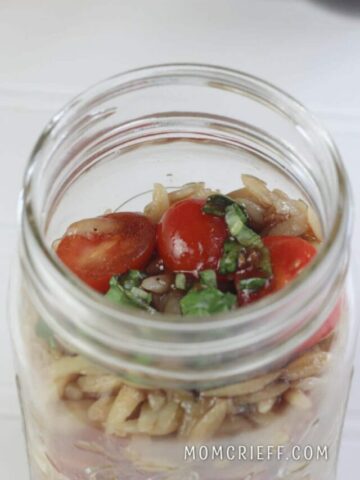 jar full of orzo pasta salad with bright tomatoes, basil and orzo