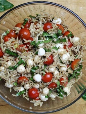 caprese orzo salad with fresh tomatos, basil, small mozzarella and orzo all in a glass bowl.