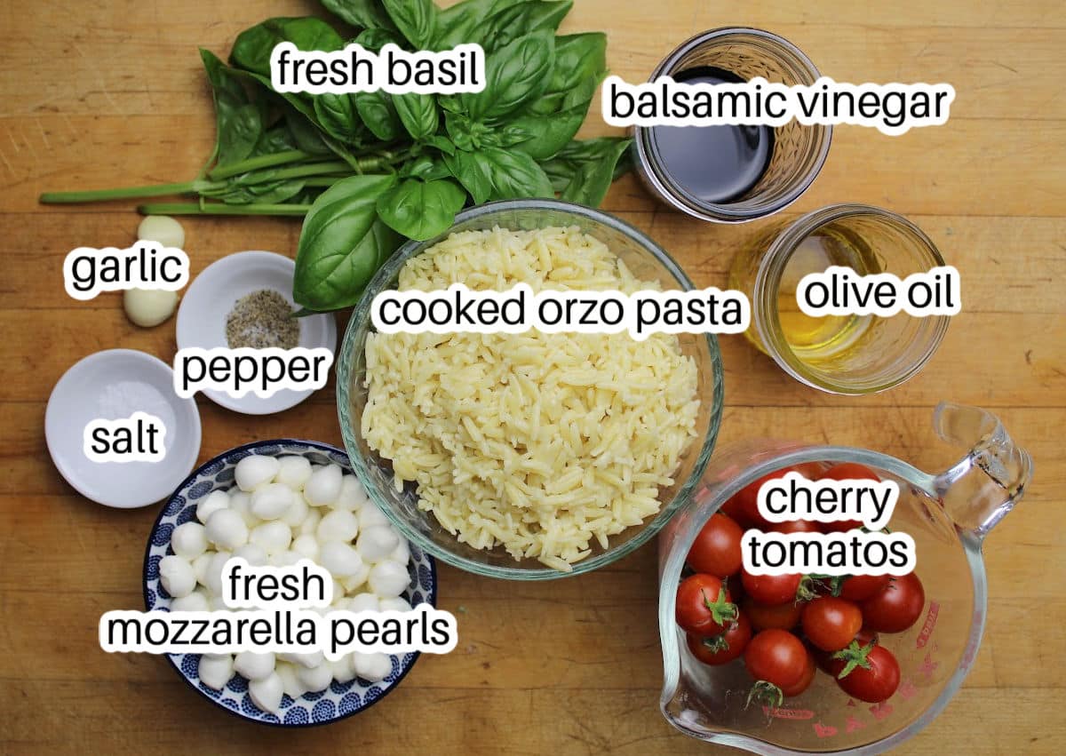 Ingredients for orzo pasta salad with orzo, cherry tomatos, fresh basil, fresh mozzarella pearls and dressing ingredients.