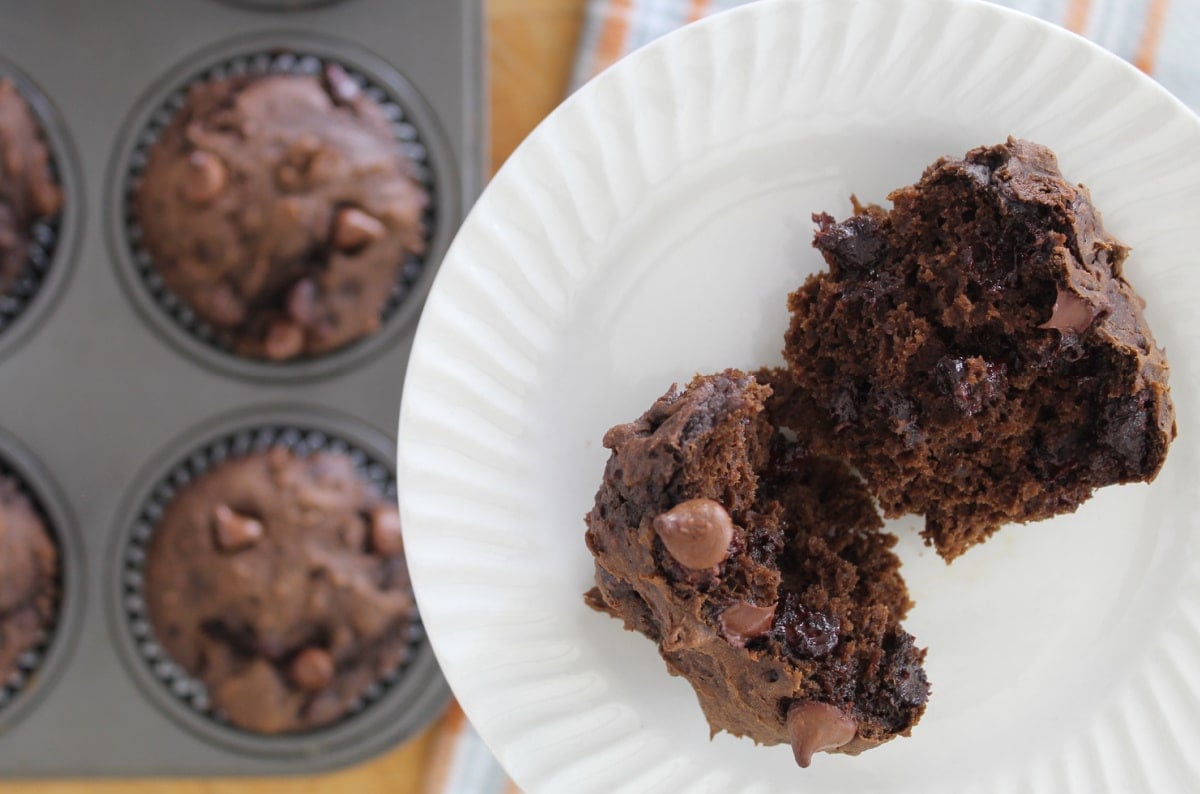 freshly baked chocolate chip pumpkin muffins in the background with a broken muffin on a white plate.