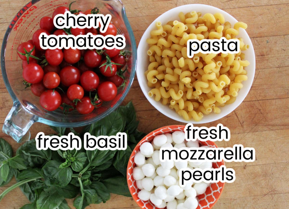 Caprese pasta salad ingredients including cherry tomatoes, pasta, mozzarella pearls and fresh basil.