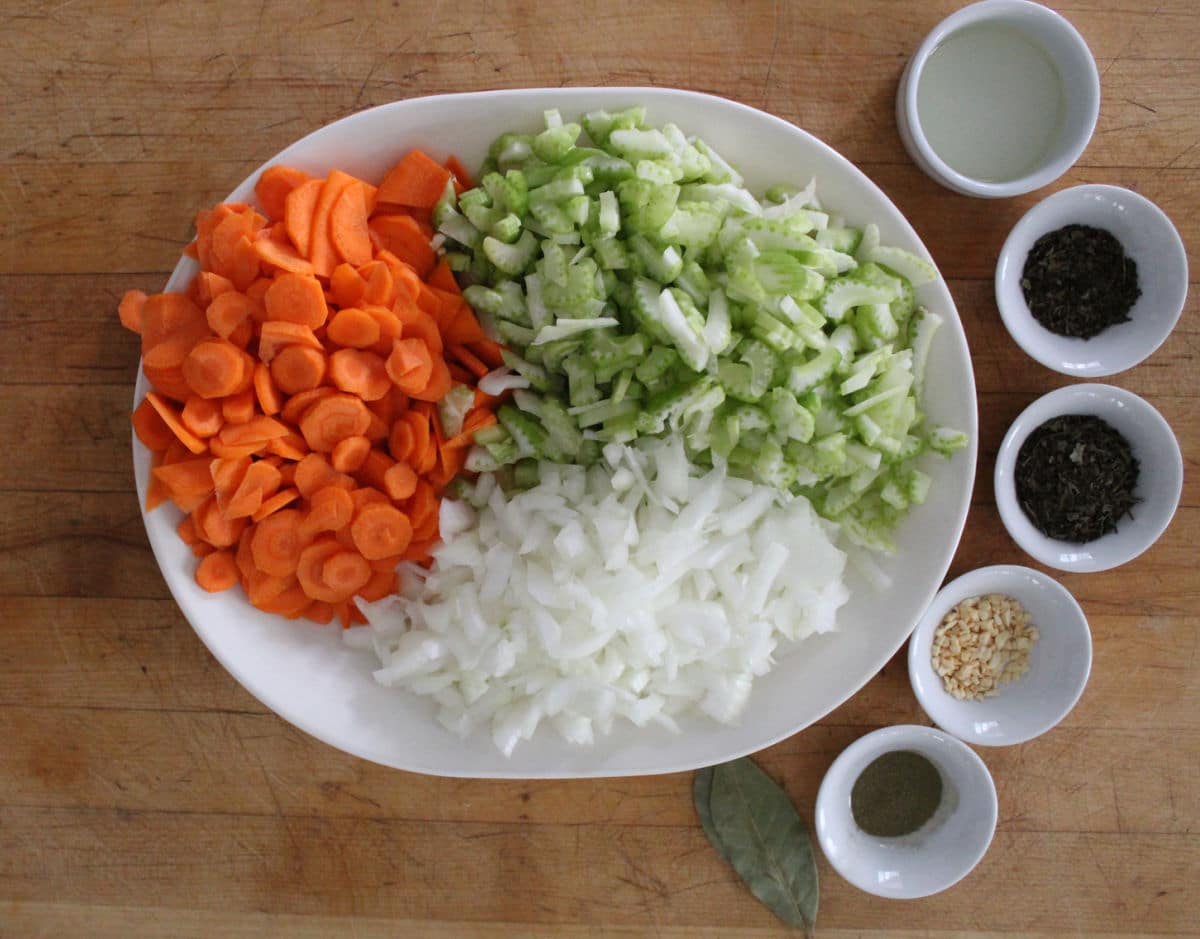 chopped carrots, celery and onions on a white plate.  Small dishes containing seasonings beside the plate.