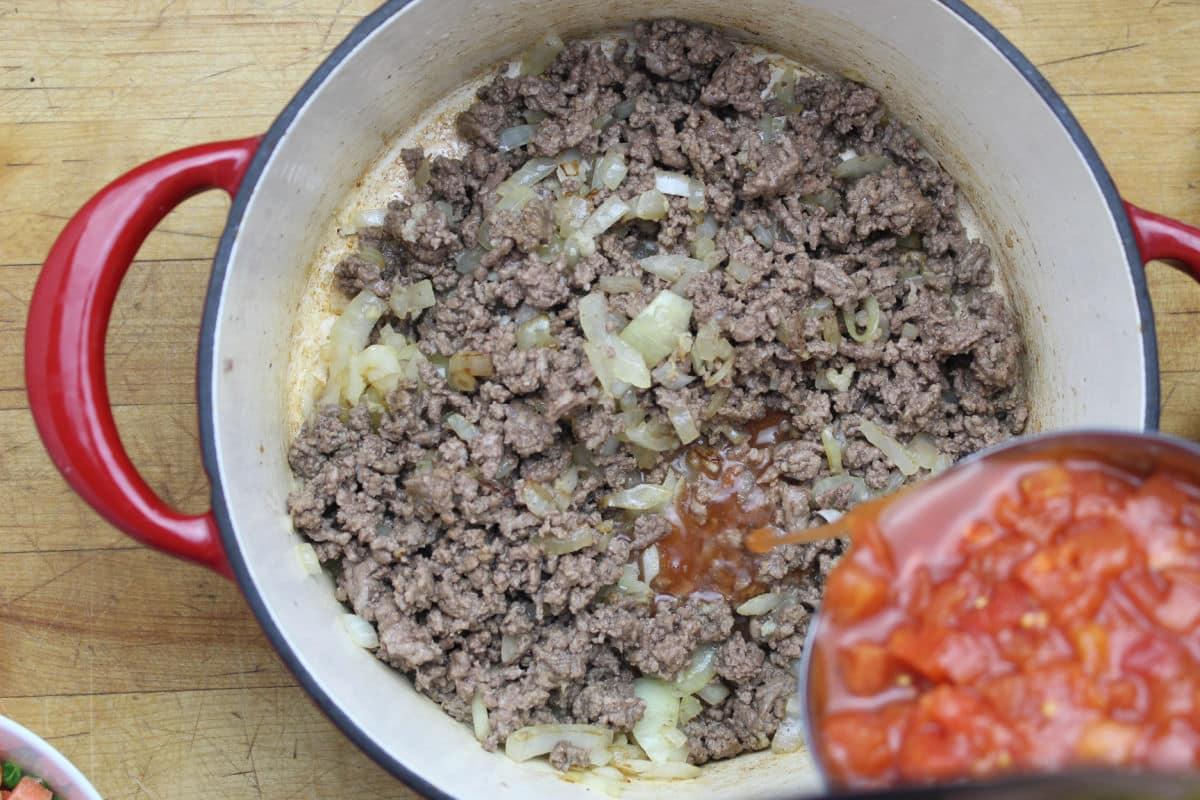Cooked hamburger with cooked diced onions with diced tomatoes being added.