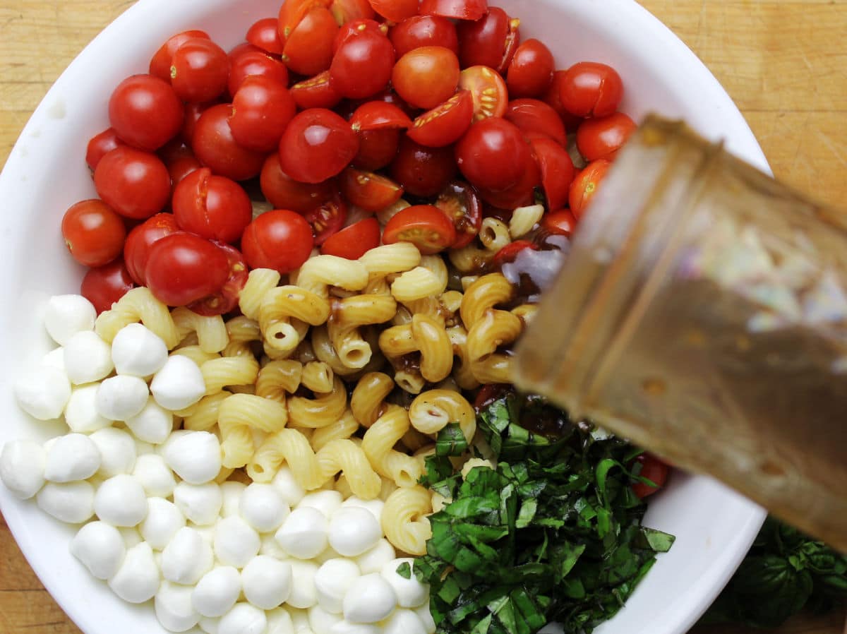 dressing being poured onto caprese pasta salad.
