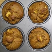 four pumpkin apple muffins with pieces of apple visible.