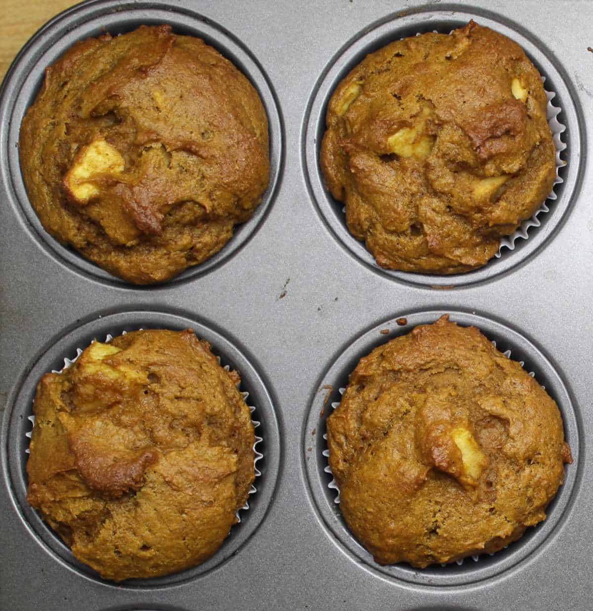 four pumpkin apple muffins with pieces of apple visible.