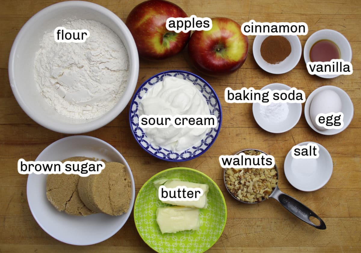 Ingredients for apple bars including flour, brown sugar, butter, sour cream, cinnamon, baking soda, walnuts, salt, egg, vanilla extract and apples.