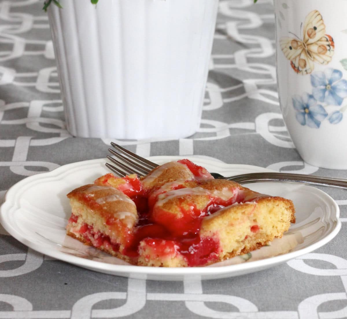 cherry pie square on a table with a gray table cloth and a cup of tea.