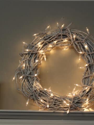 White Christmas wreath with white lights on a shelf.