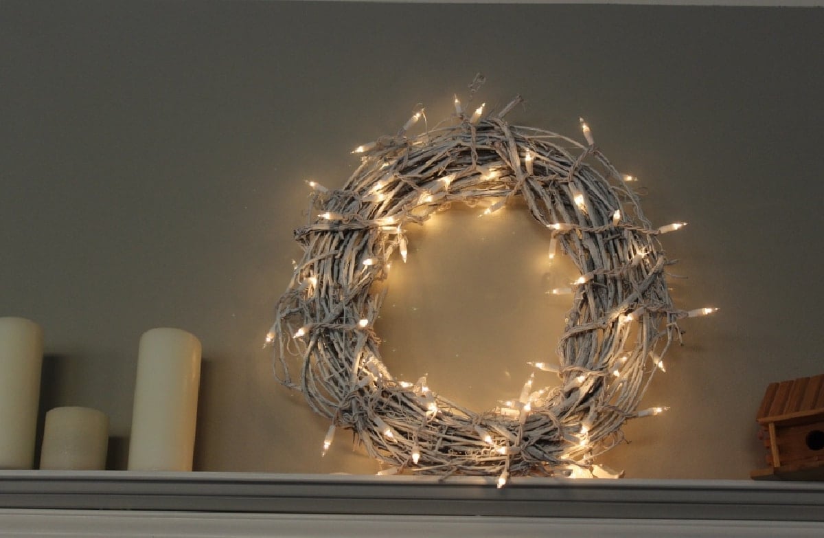 White Christmas wreath with white lights on a shelf.