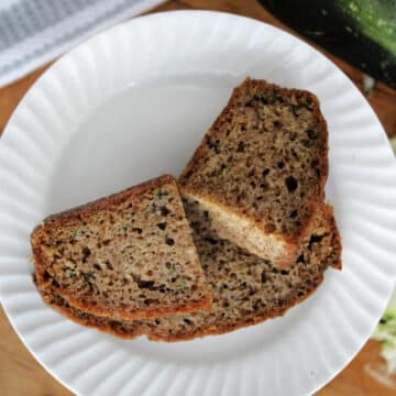 Two slices of zucchini bread on a white plate with shredded zucchini in the background.