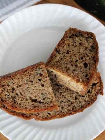 Two slices of zucchini bread on a white plate with shredded zucchini in the background.