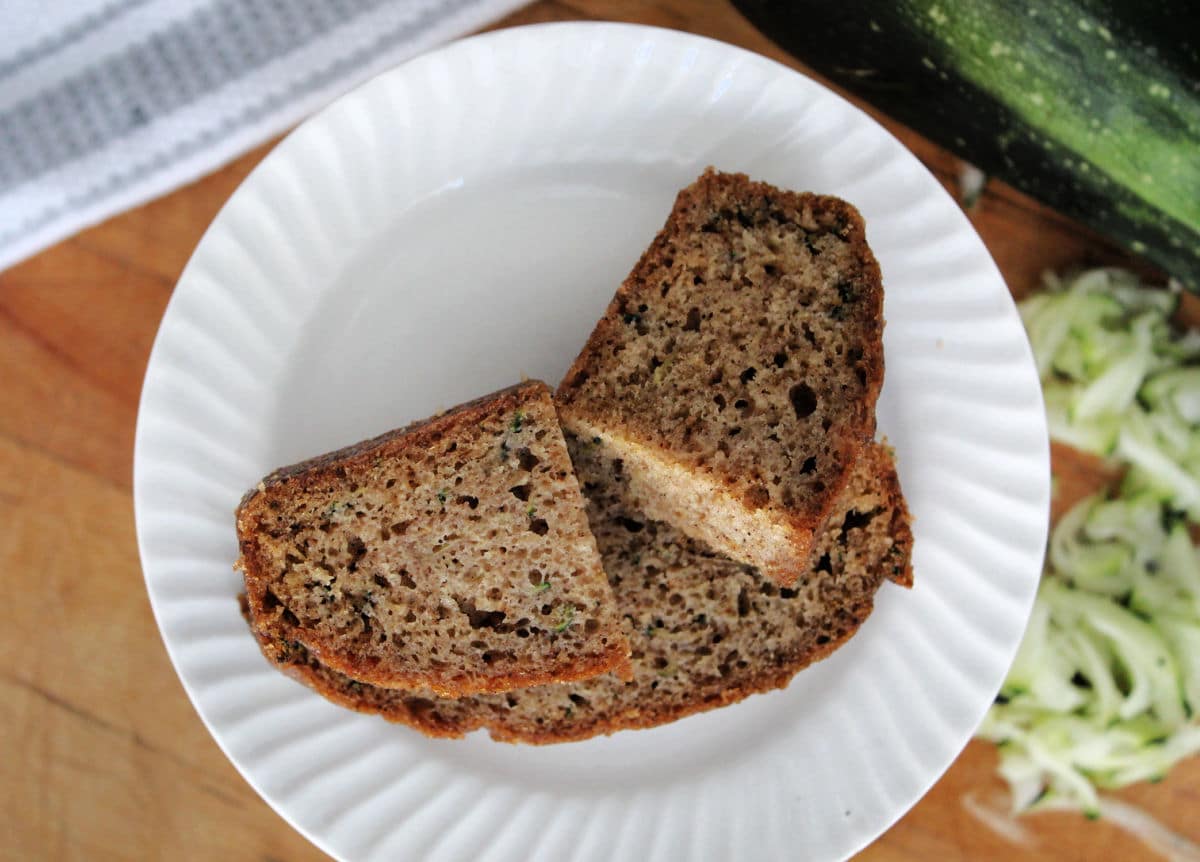 Two slices of zucchini bread on a white plate with shredded zucchini in the background. 