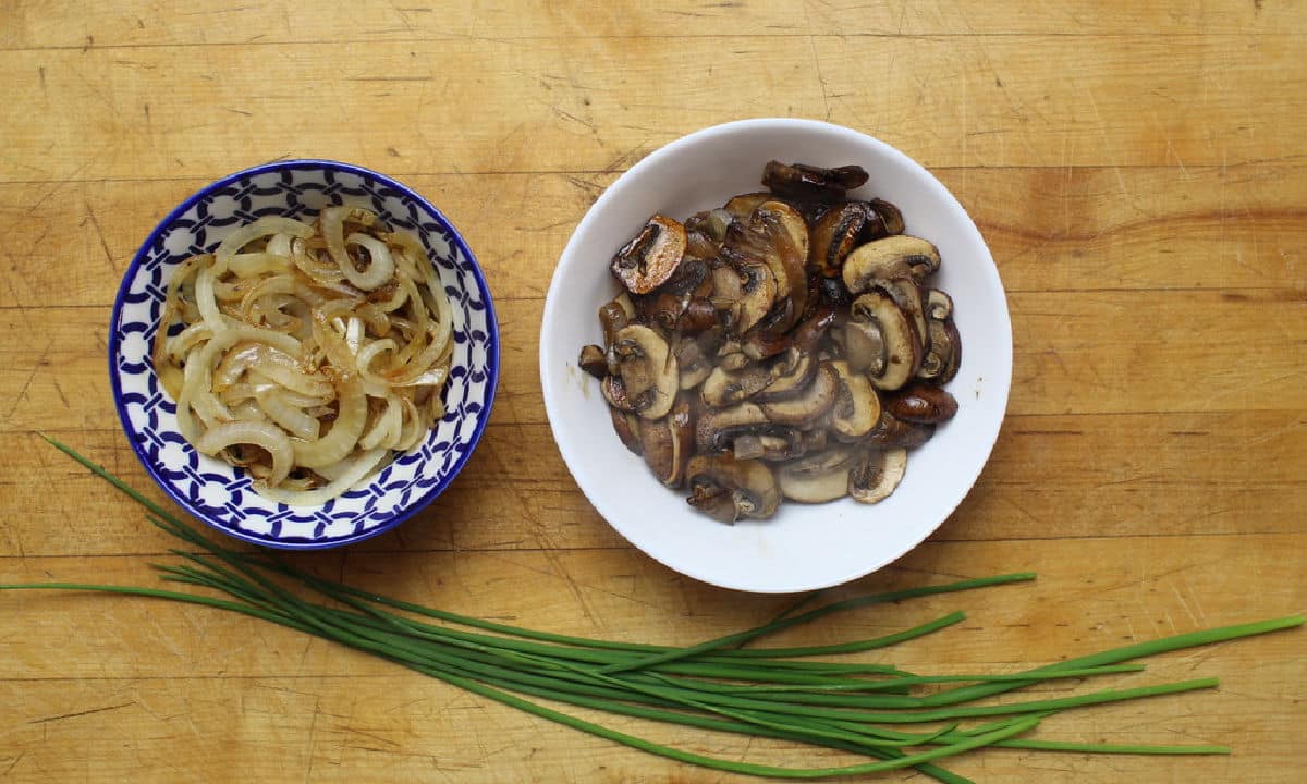seperate bowls of sauteed onions and mushrooms with chives laying below the bowls.