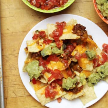 plate of nachos covered with ground beef, cheese, salsa and guacamole.