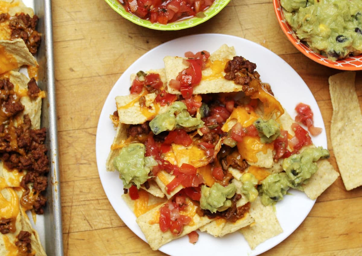 plate of nachos covered with ground beef, cheese, salsa and guacamole.