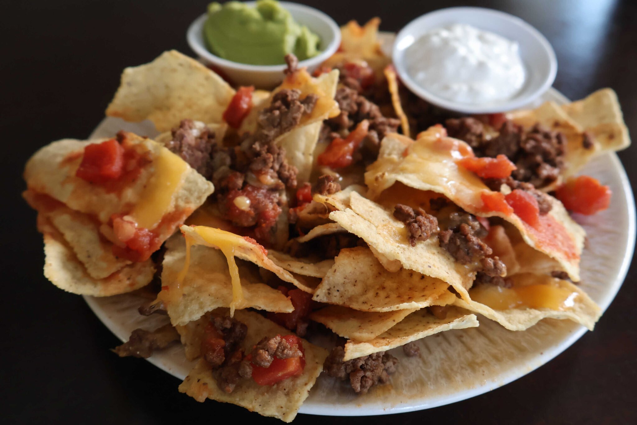 plate with ground beef nachos with melted cheese.  guacamole and sour cream served in small containers to dip.