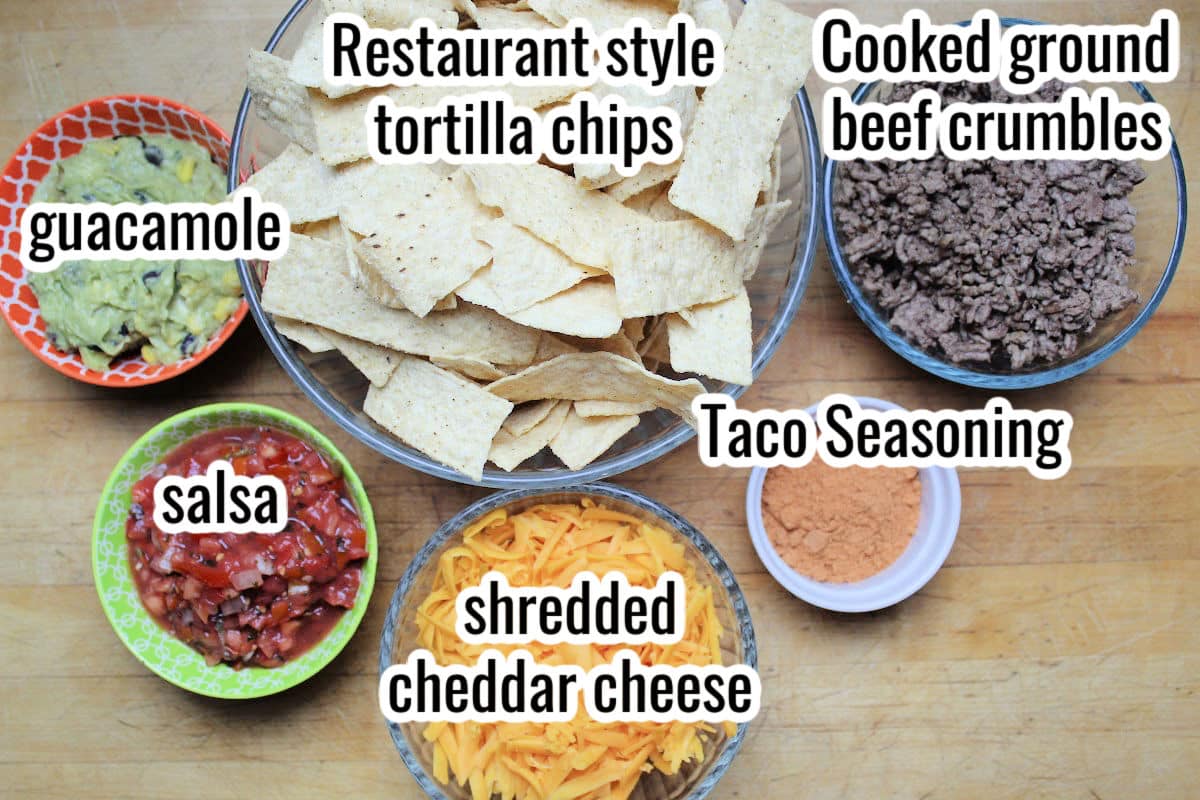 Ingredients for beef nachos insluding tortilla chips, ground beef crumbles, guacamole, salas, shredded chedar cheese, taco seasoning
