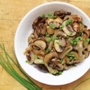 Sautéed onions and mushrooms topped with a sprinkle of chopped chives in a white bowl