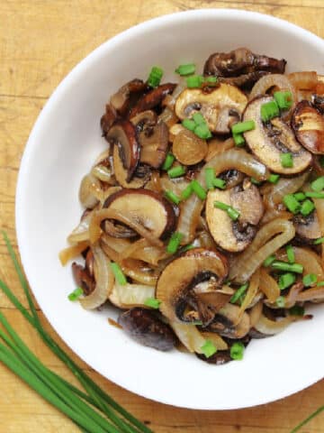 Sautéed onions and mushrooms topped with a sprinkle of chopped chives in a white bowl