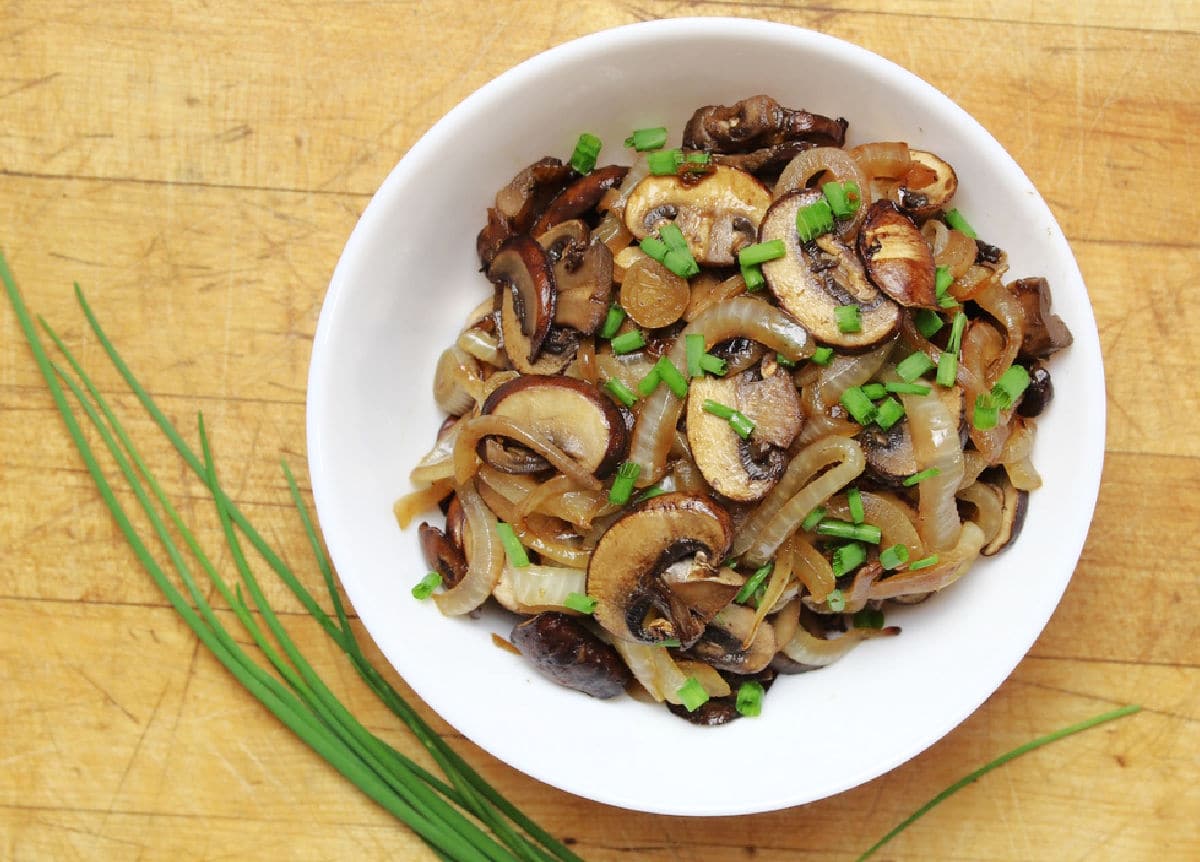 Sautéed onions and mushrooms topped with a sprinkle of chopped chives in a white bowl
