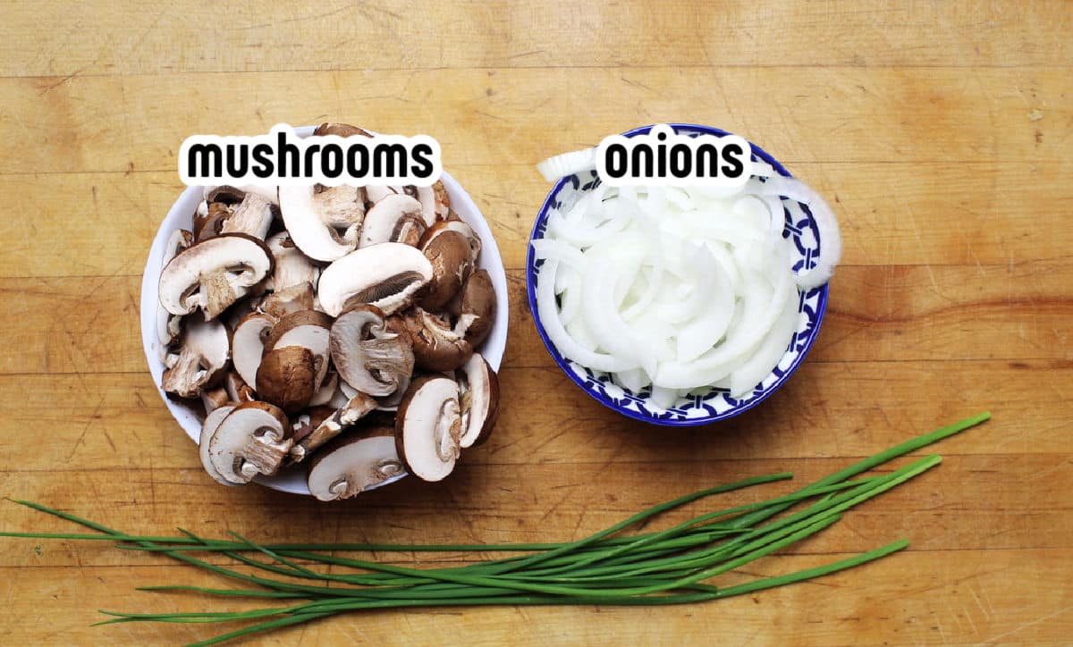 sliced mushrooms and onions in separate bowls with chives lying below.