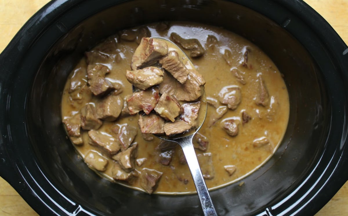 Beef tips with gravy on a serving spoon, above a slow cooker full of beef and gravy!